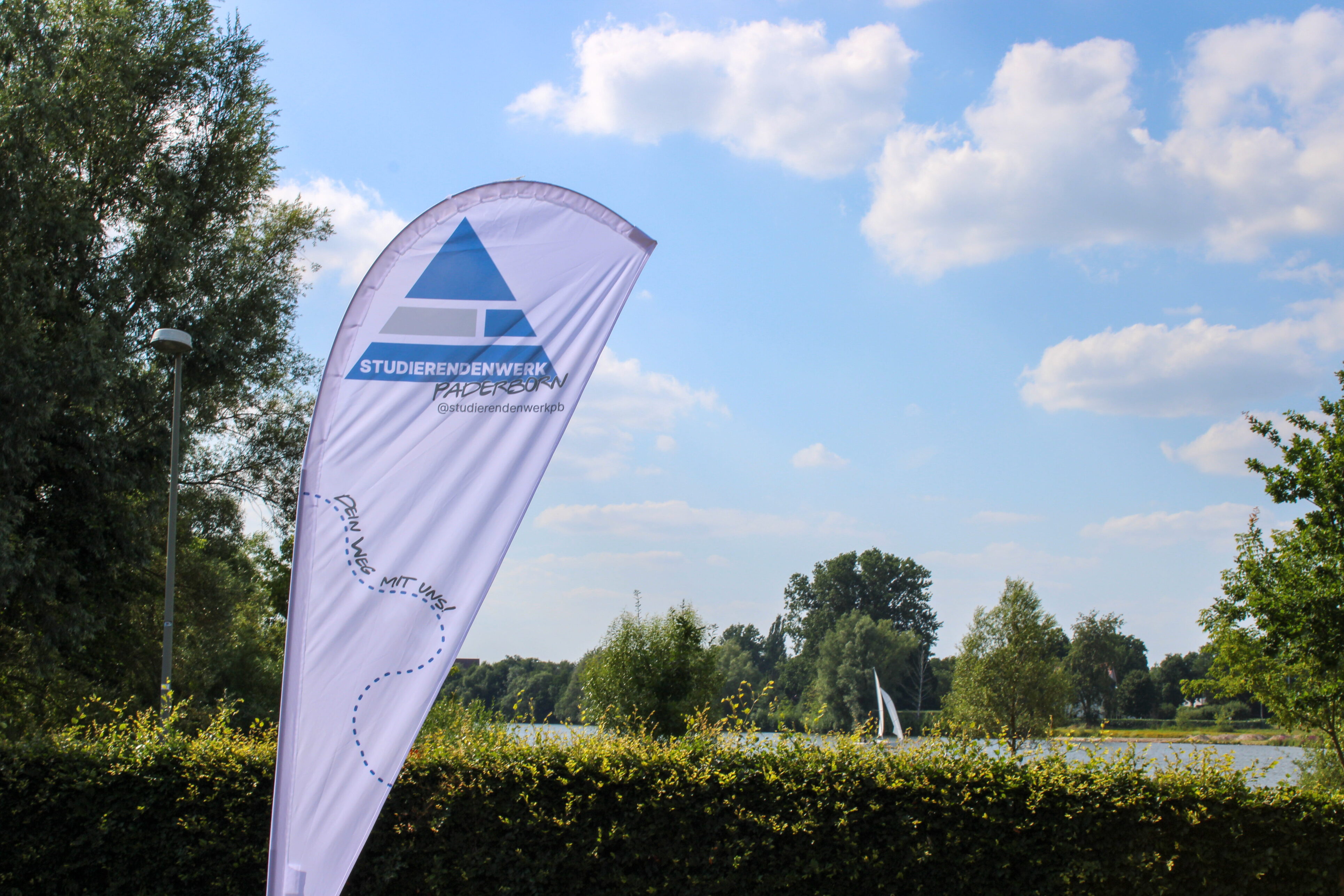 White beach flag with the blue Studierednenwerk logo in the shape of a triangle