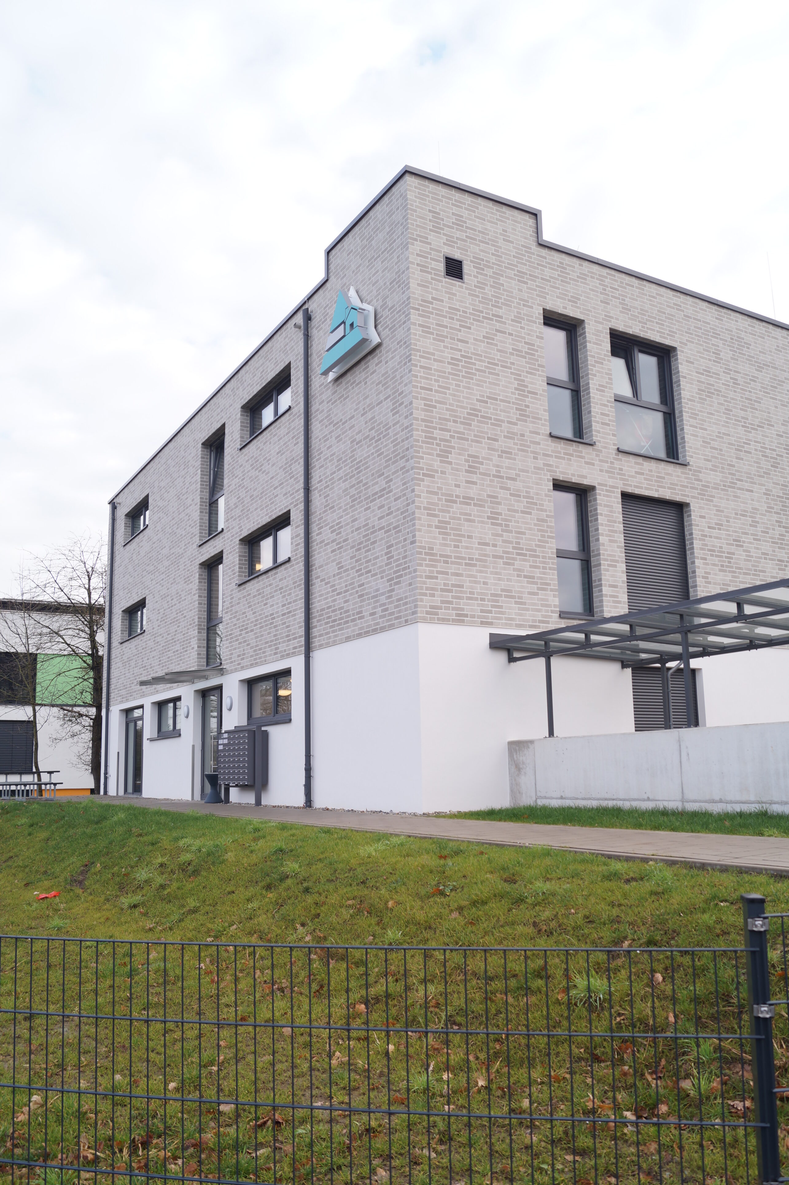 Eckansicht mit Blick auf den Eingangsbereich eines Gebäudes mit moderner Architektur und dem Dreieck-Logo des Studierendenwerks Paderborn an einer Seite der Fassade.