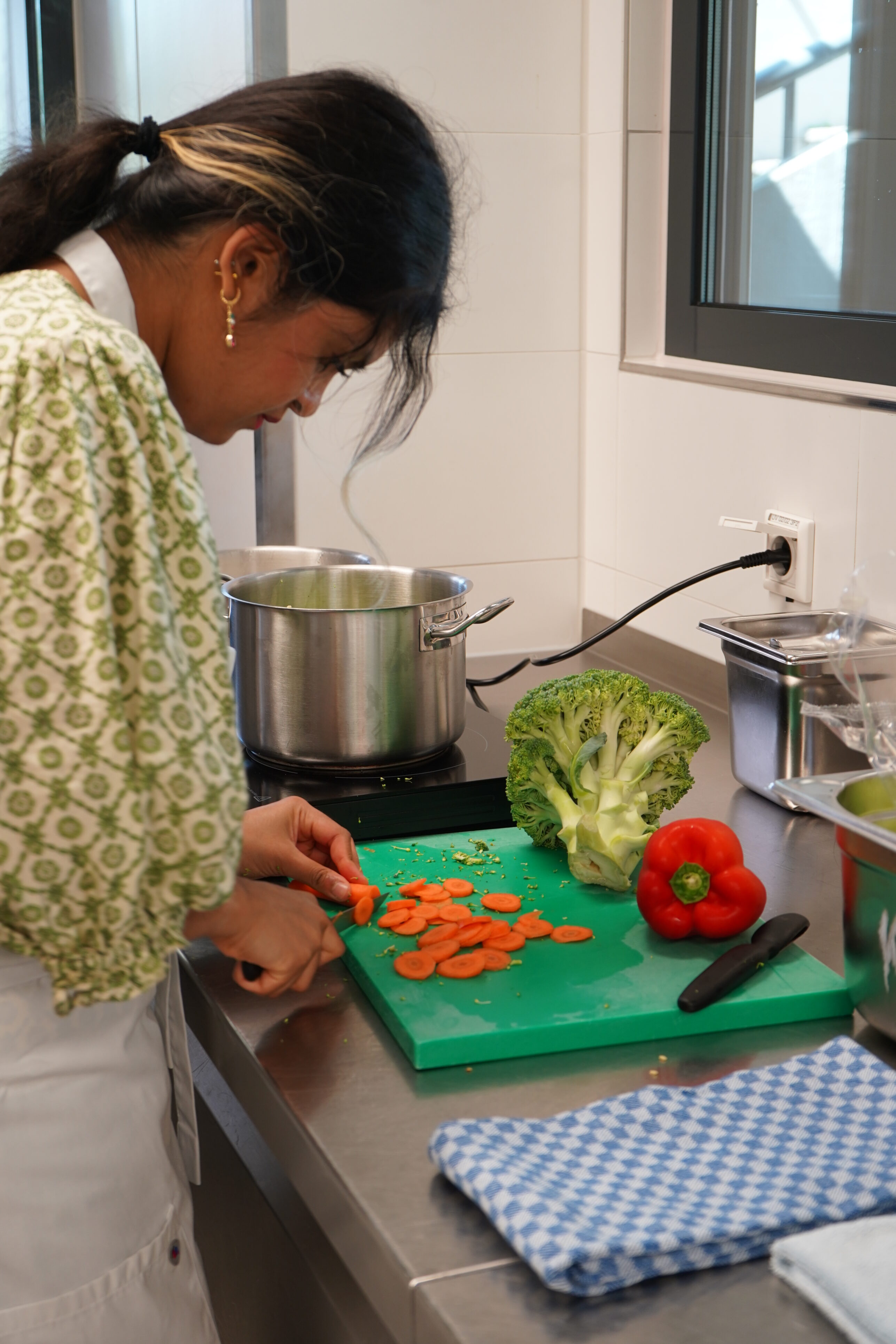 A person is cutting a carrot. Next to it are a pepper and some broccoli.