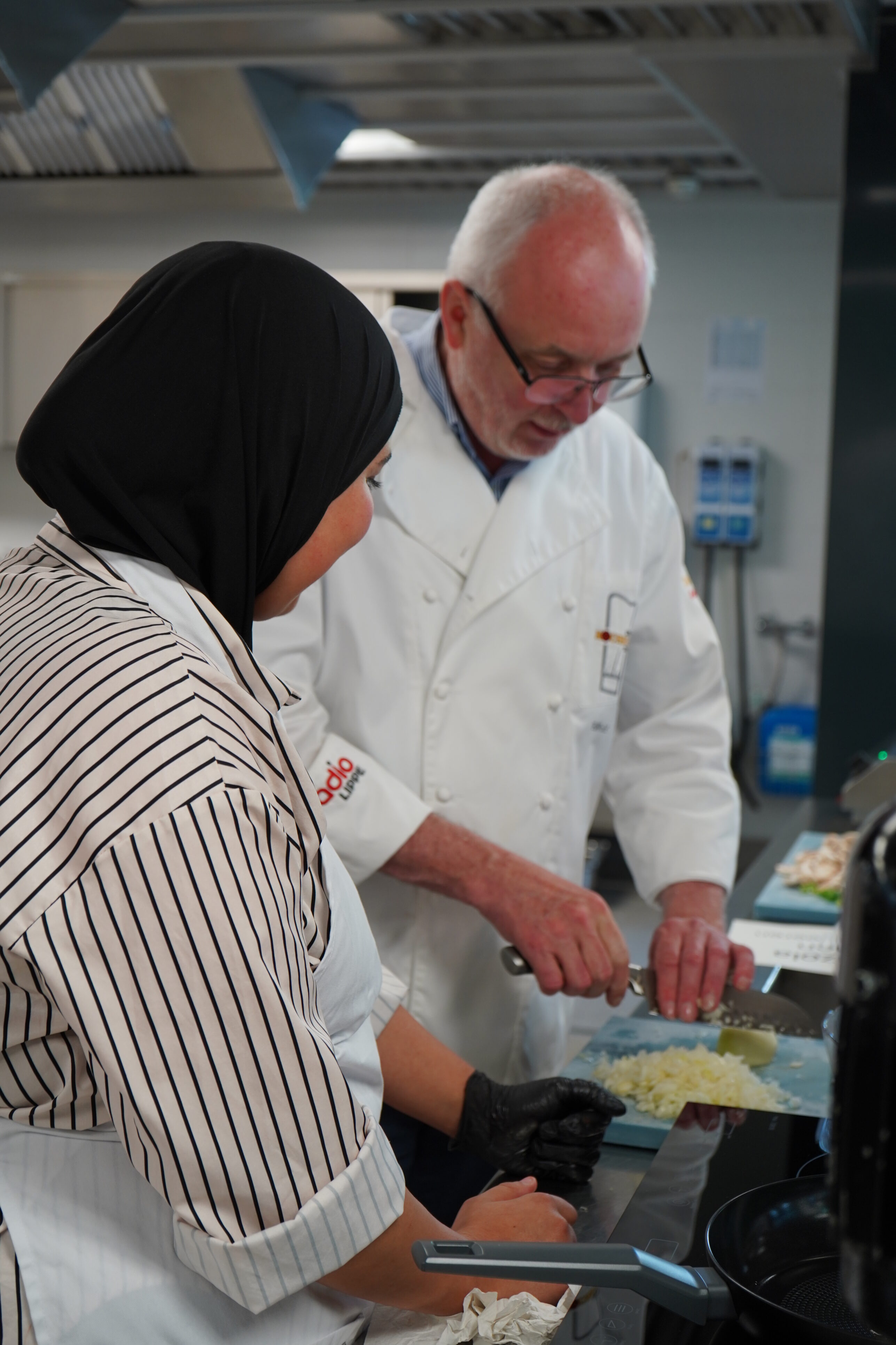 Two people are standing facing each other. One of them is chopping an onion