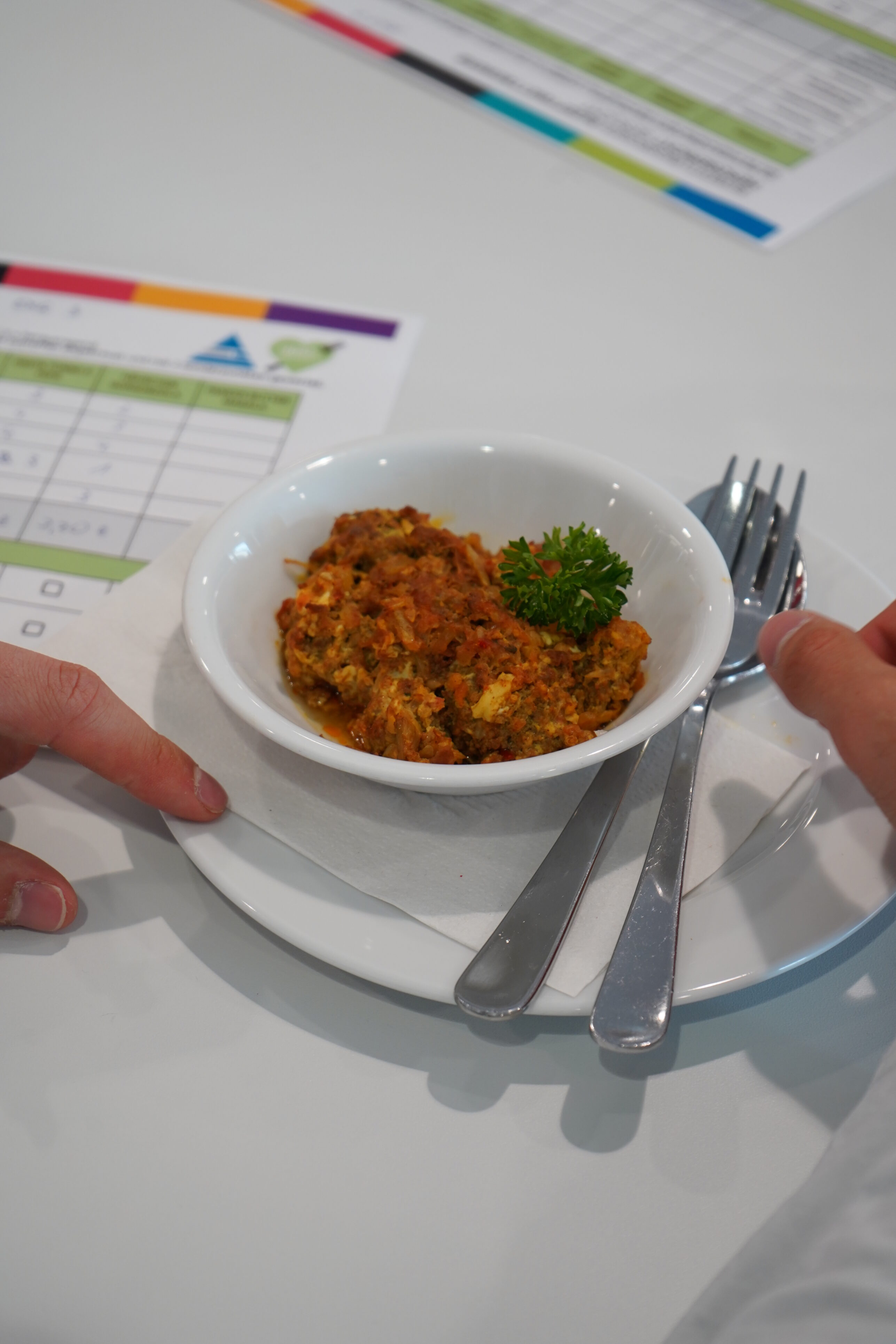 A small bowl of food. Next to it are a fork, a spoon and a feedback form.
