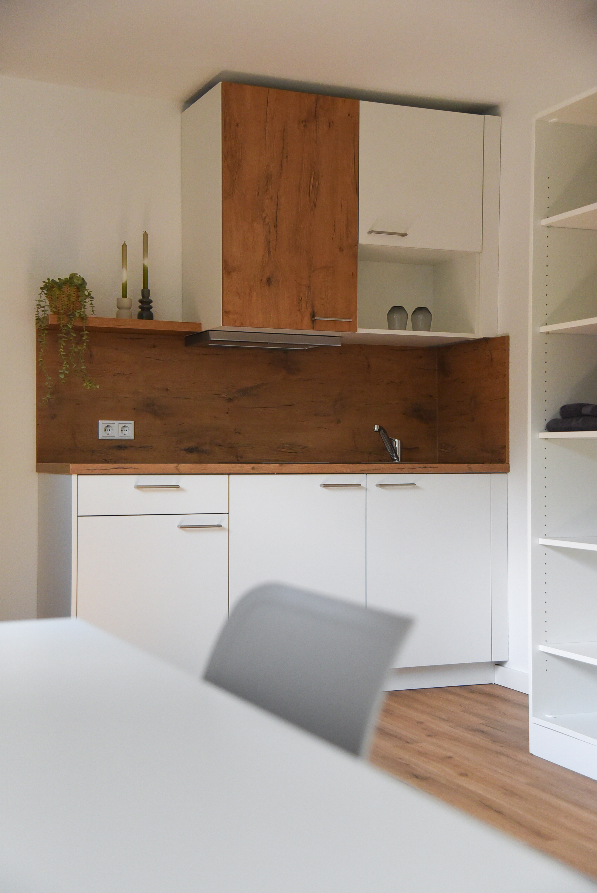 A modern kitchen unit with white fronts and a worktop and splashback in a wood look.