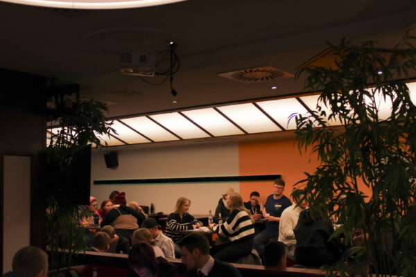 Viele Menschen sitzen an den Tischen in einem Raum. Sie lachen und unterhalten sich.