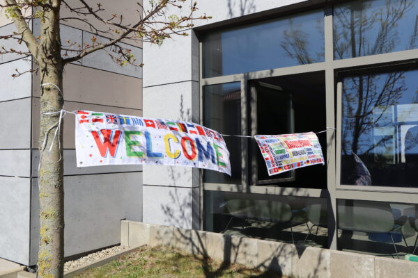 Ein Banner mit dem Wort Welcome ist zwischen einem Baum und einem offenen Fenster im Erdgeschoss eines Gebäudes gespannt