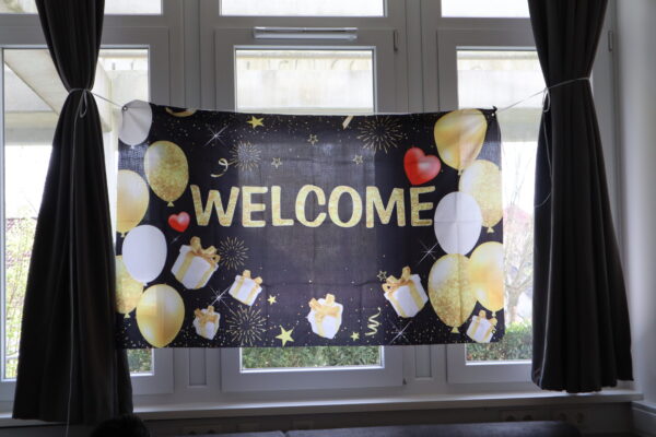 Vor dem Fenster hängt ein Banner auf dem Luftballons und die Aufschrift "Welcome" gedruckt sind.