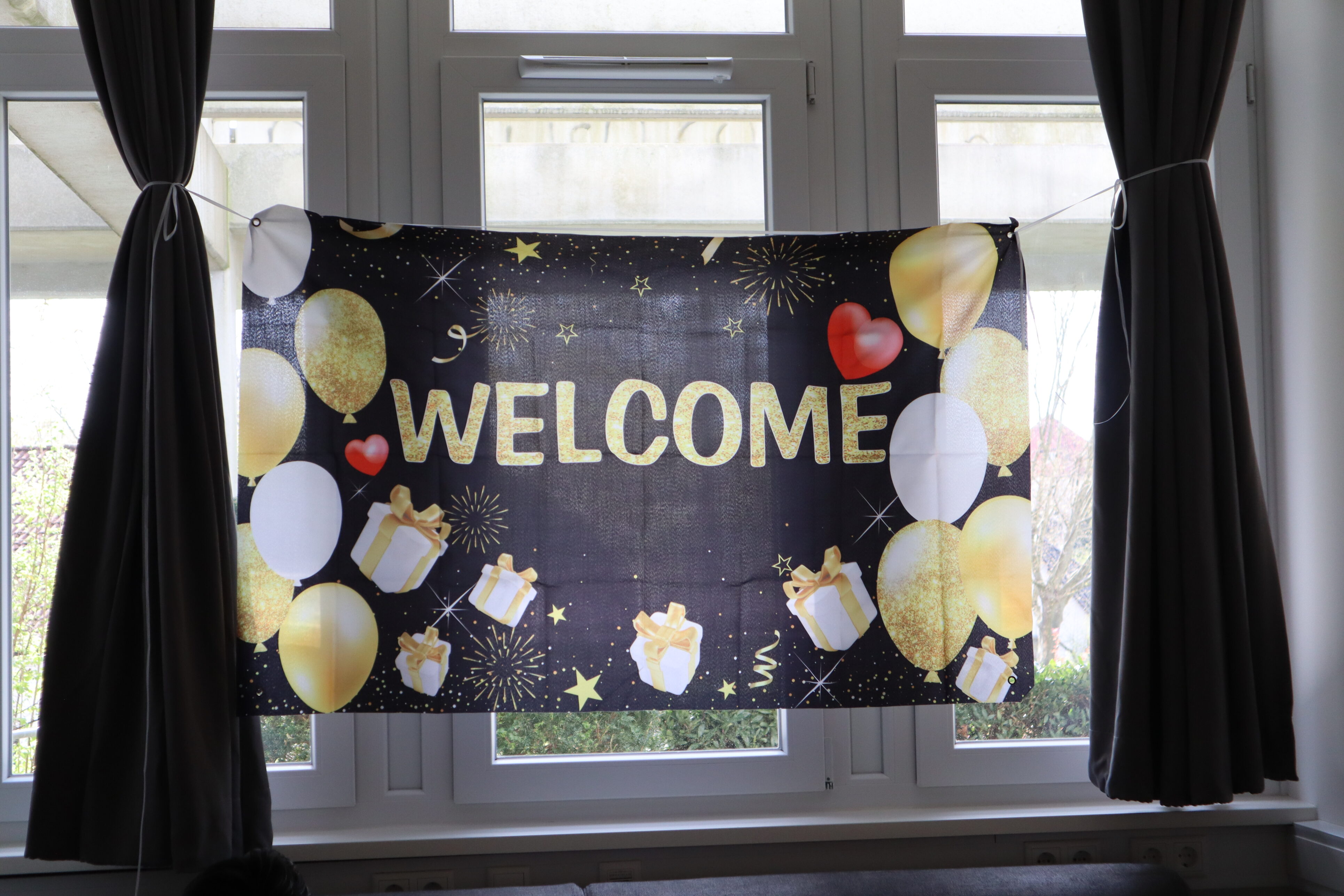 Vor dem Fenster hängt ein Banner auf dem Luftballons und die Aufschrift "Welcome" gedruckt sind.