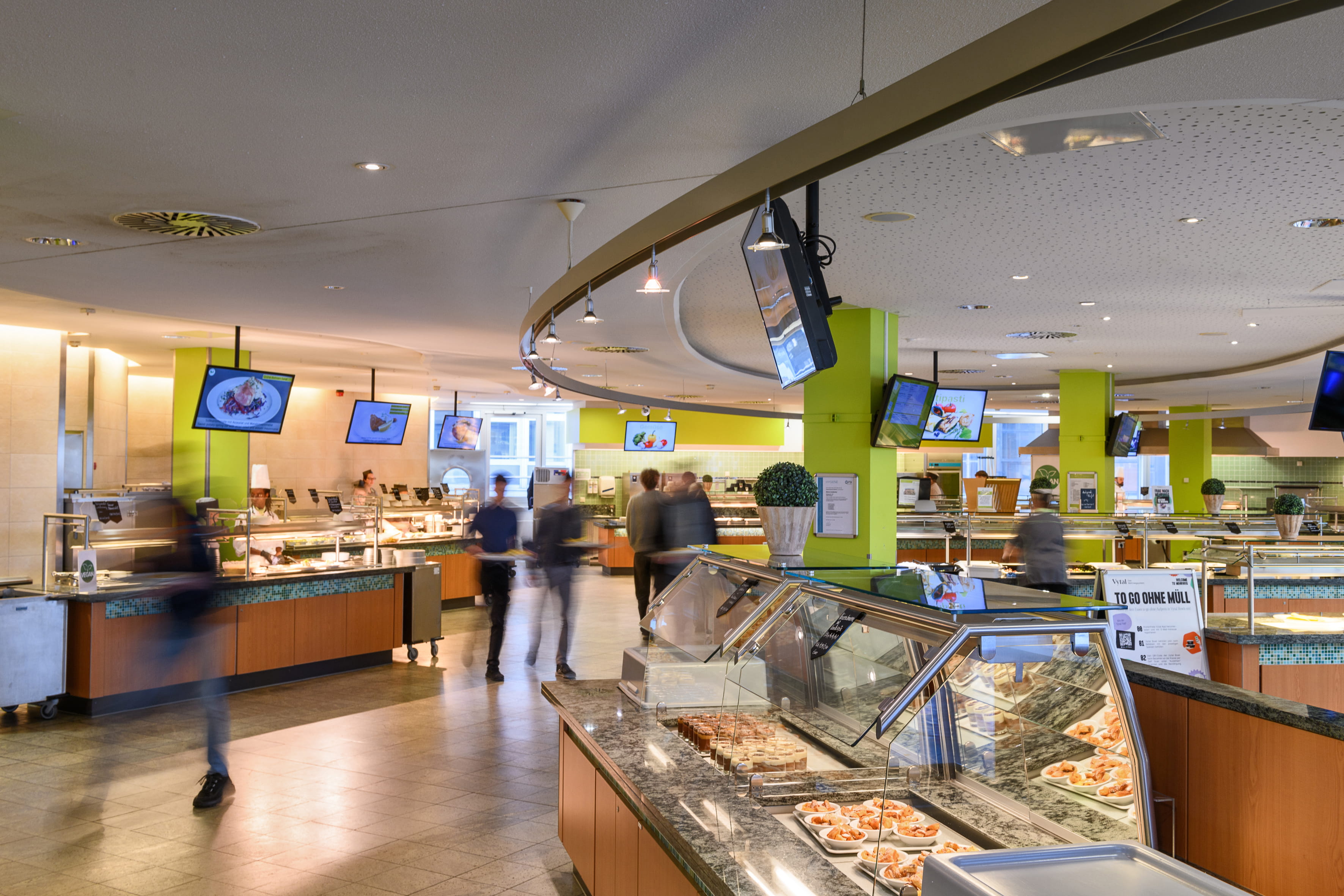 Die Essenausgaben einer Mensa, zwischen denen die Gäste hin und her laufen