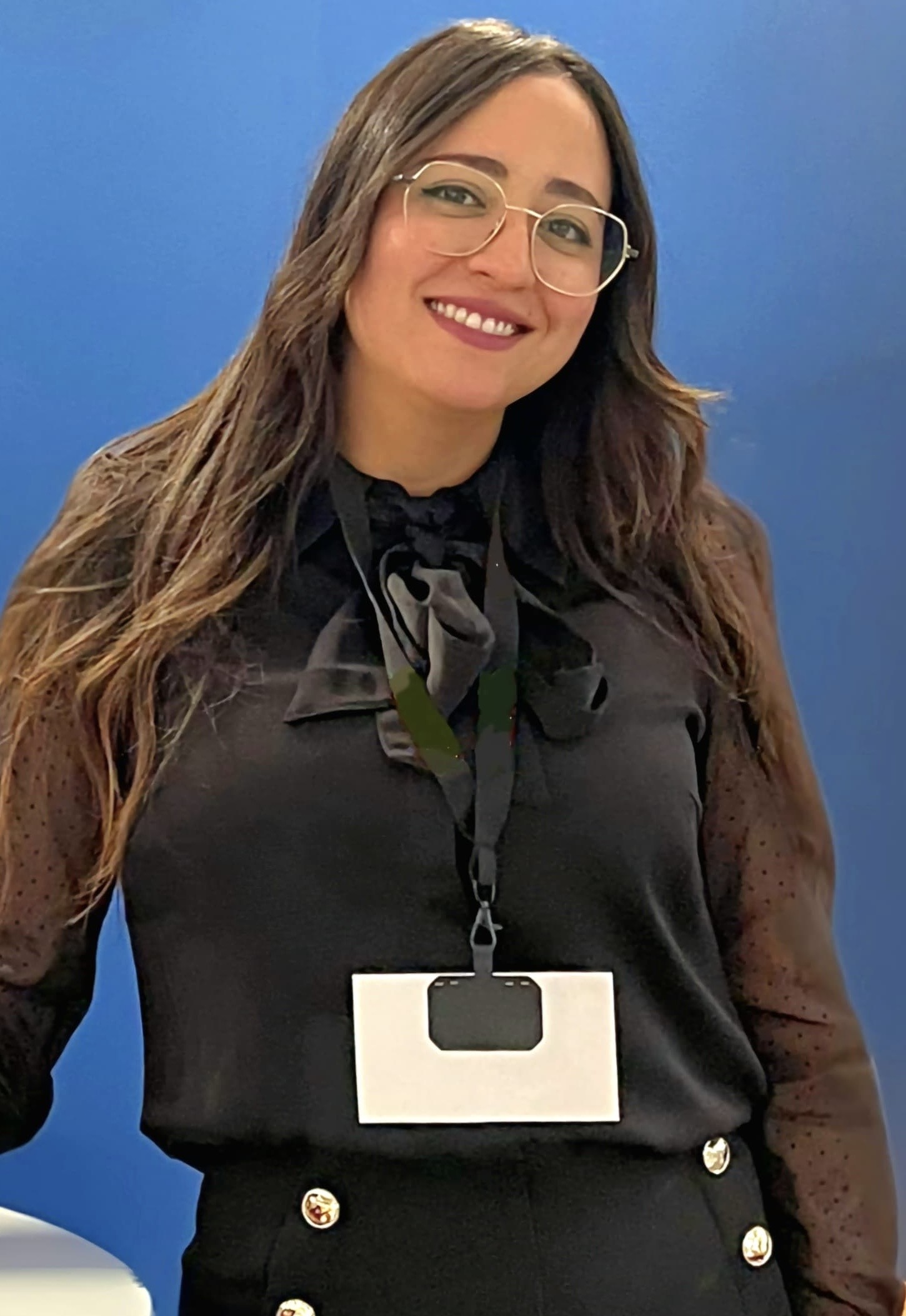 Eine weibliche Person mit langen dunklen Haaren und Brille lächelt in die Kamera