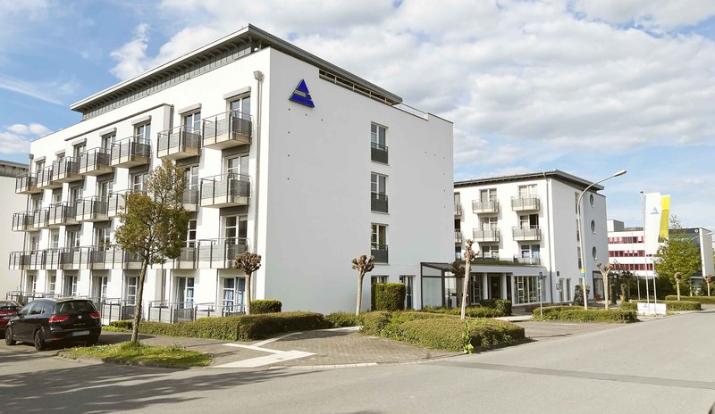 The photo shows the administrative building of the Paderborn Student Union. The blue Studierendenwerk logo in the form of a triangle is depicted on the wall of the building.