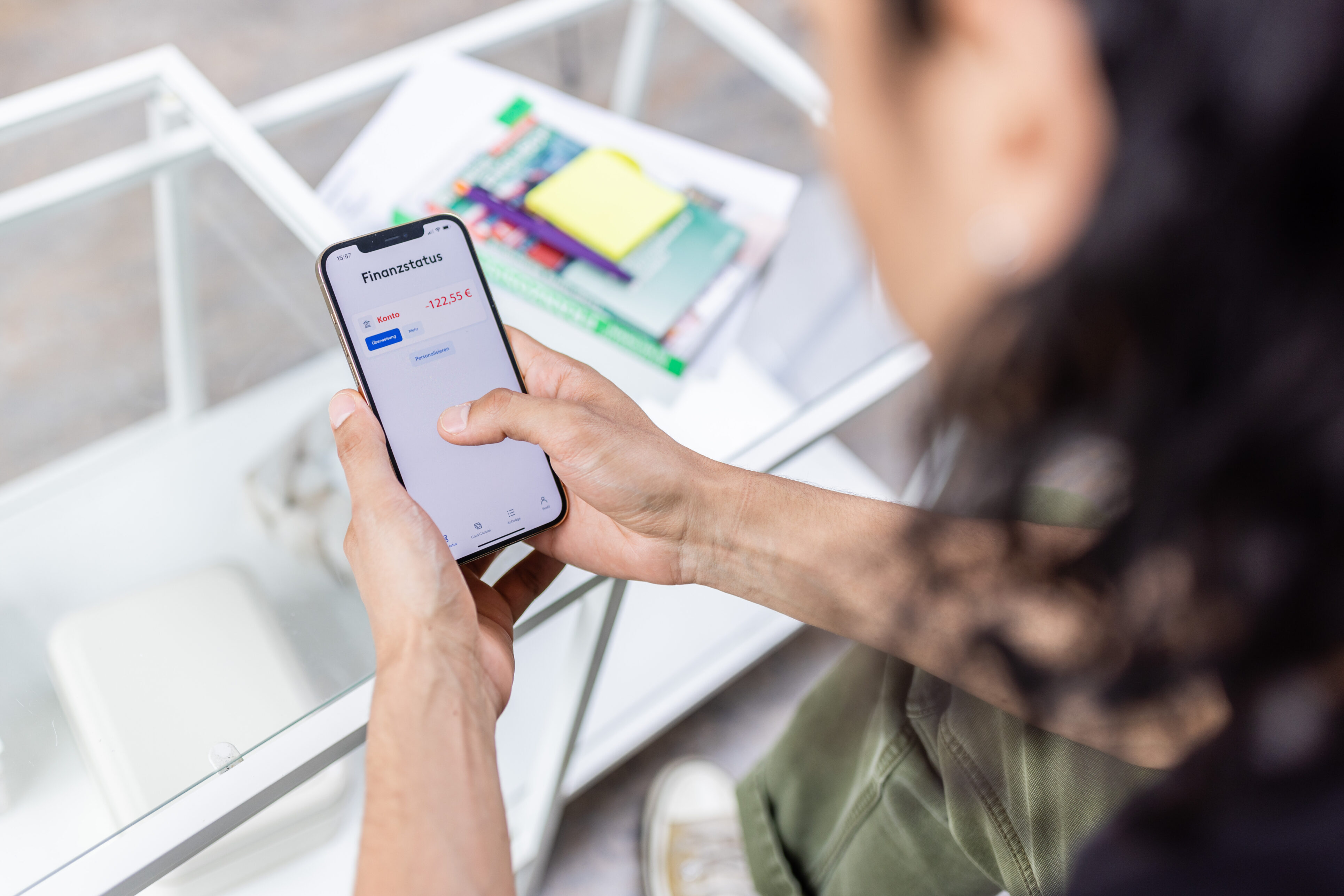 Eine Person hält ein Handy in der Hand, auf dem der Finanzstatus in Höhe von -122,55€ in Rot angezeigt wird.