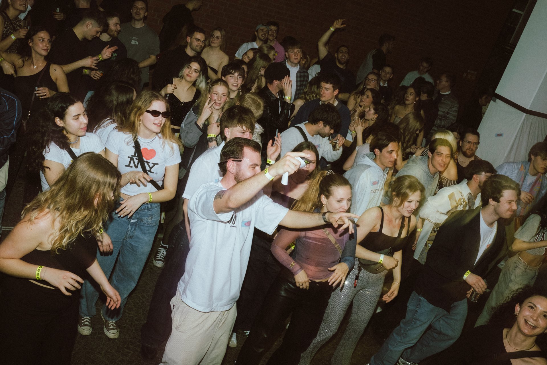 Verschiedene Personen tanzen und feiern in einer belebten Atmosphäre, umgeben von Musik und Getränken.