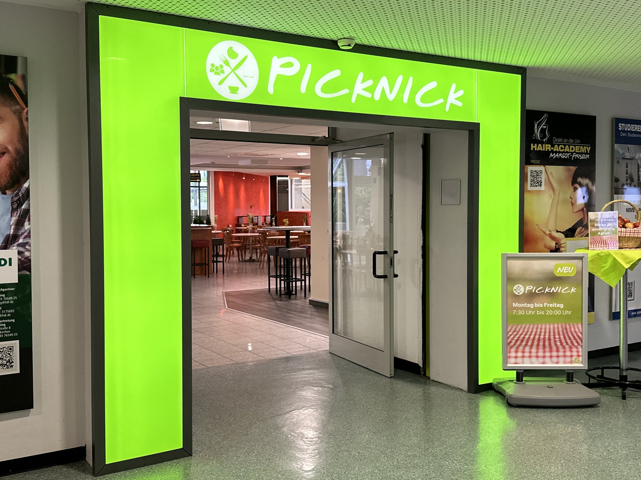 Eingang zu einem Gastronomiebereich mit dem Namen "PICKNICK", leuchtend grüne Beschilderung und Öffnungszeiten.