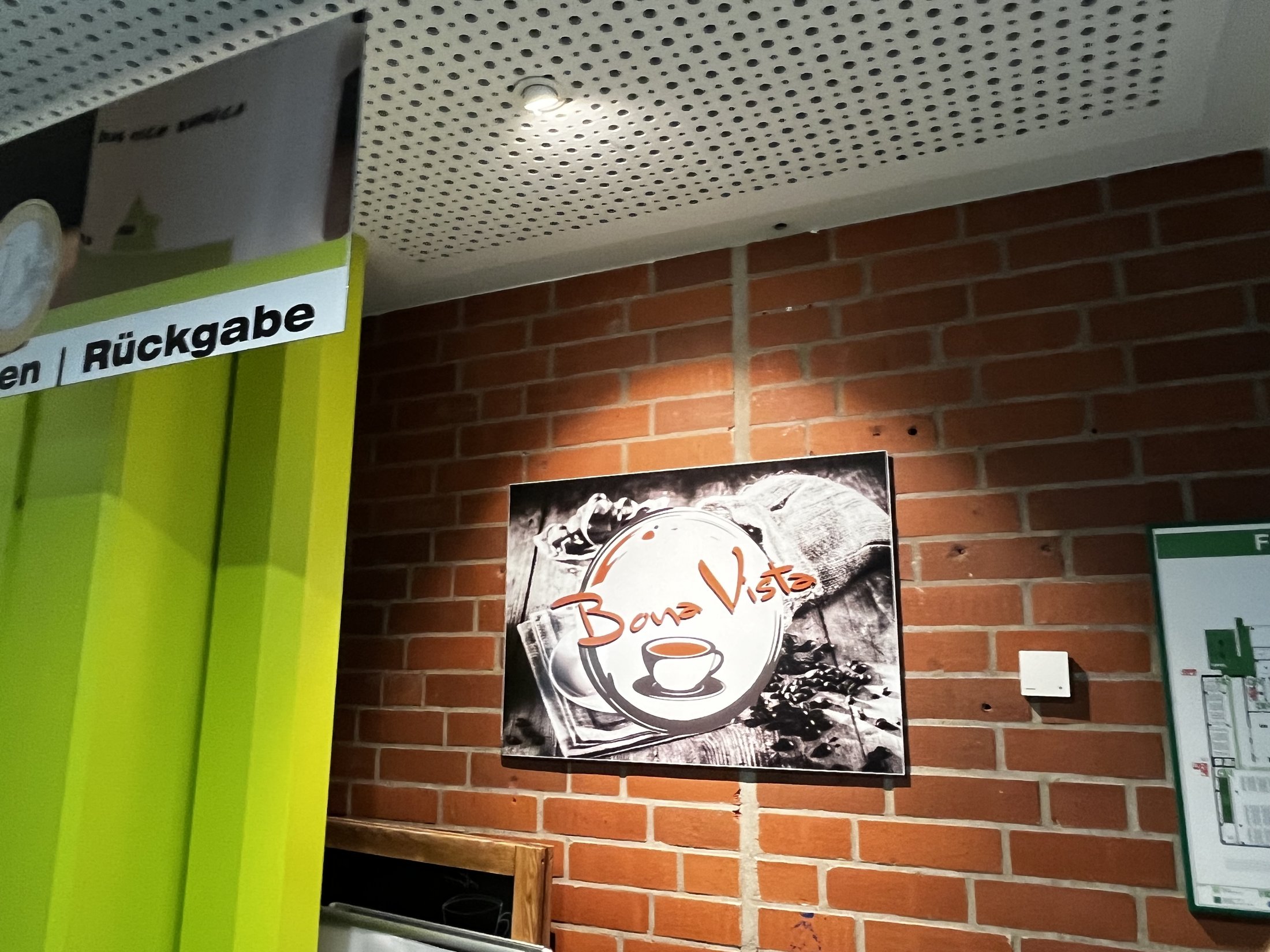 Bunte Wand mit einem Bild von Kaffee und Gebäck sowie einem Leitspruch. Im Hintergrund ist ein Stadtplan sichtbar.