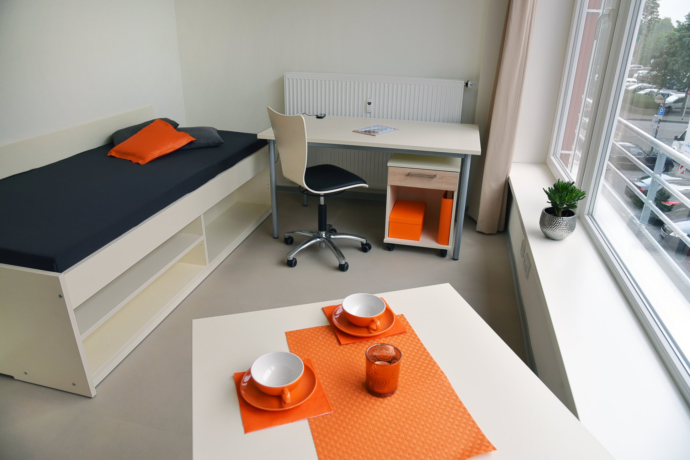 Modernes Studierendenwohnheim in Hamm mit einem Einzelzimmer, Schreibtisch und gemütlicher Sitzecke in Orange.