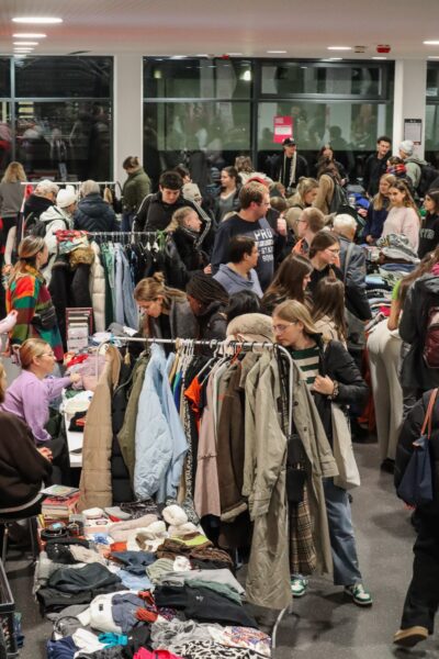 Ein großer Raum mit vielen Menschen, die durch Kleiderständer und Tische mit Kleidung stöbern.