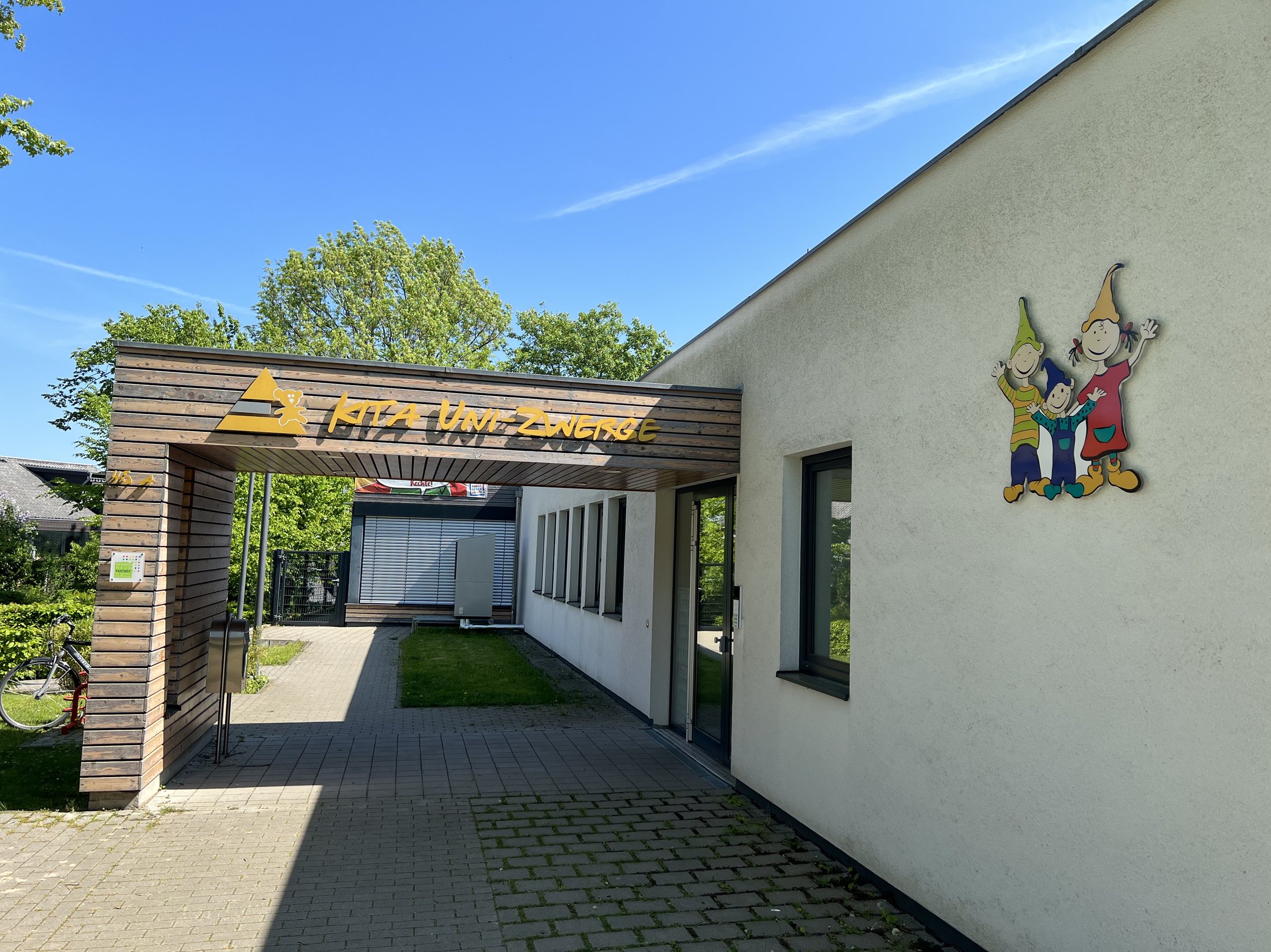 Eingangsbereich einer Kita mit Holzverkleidung und buntem Logo, begleitet von einer freundlichen Wandgestaltung.