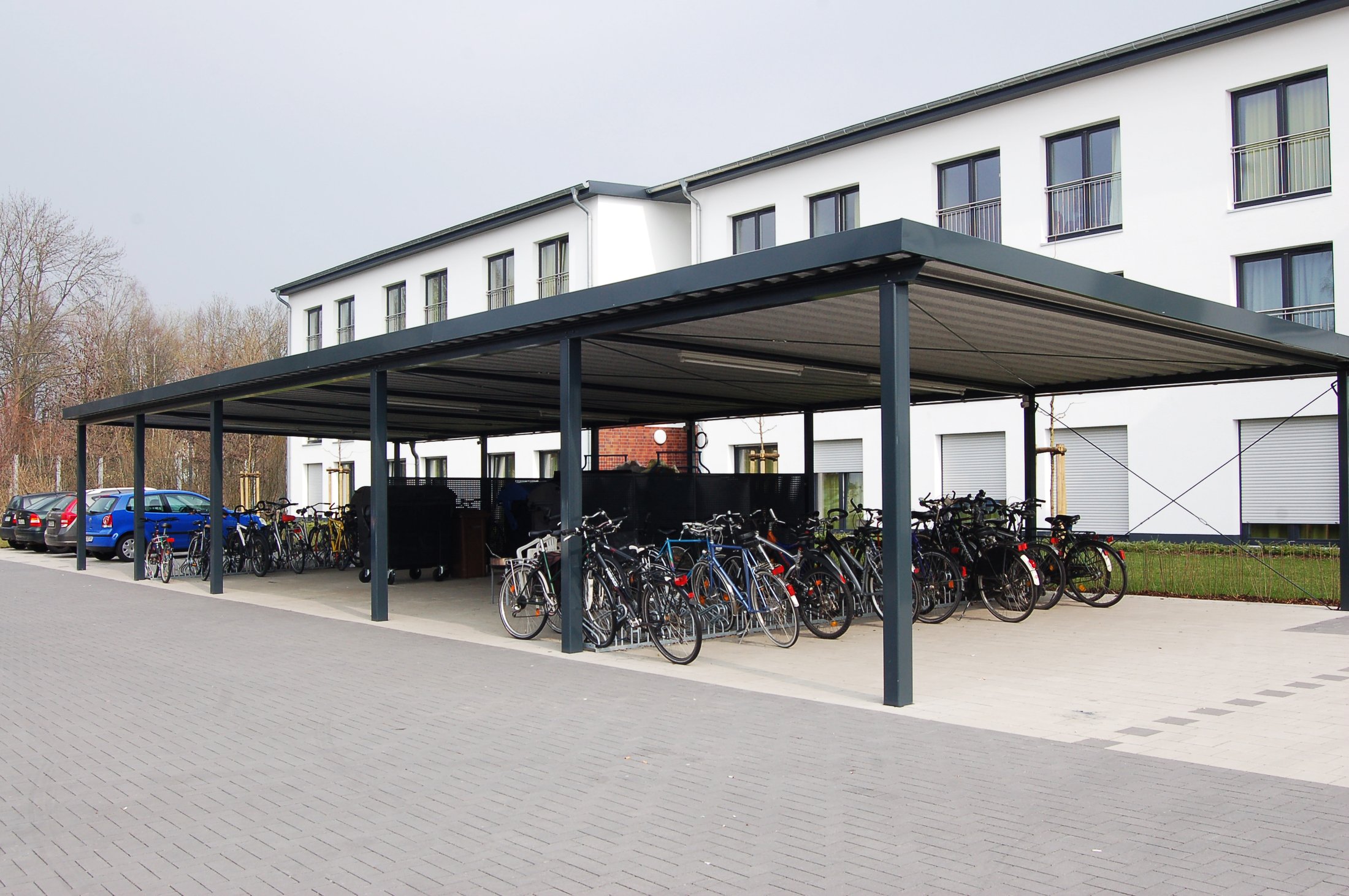 Studierendenwohnheim in Lippstadt mit überdachtem Fahrradstellplatz und parkenden Autos im Hintergrund.