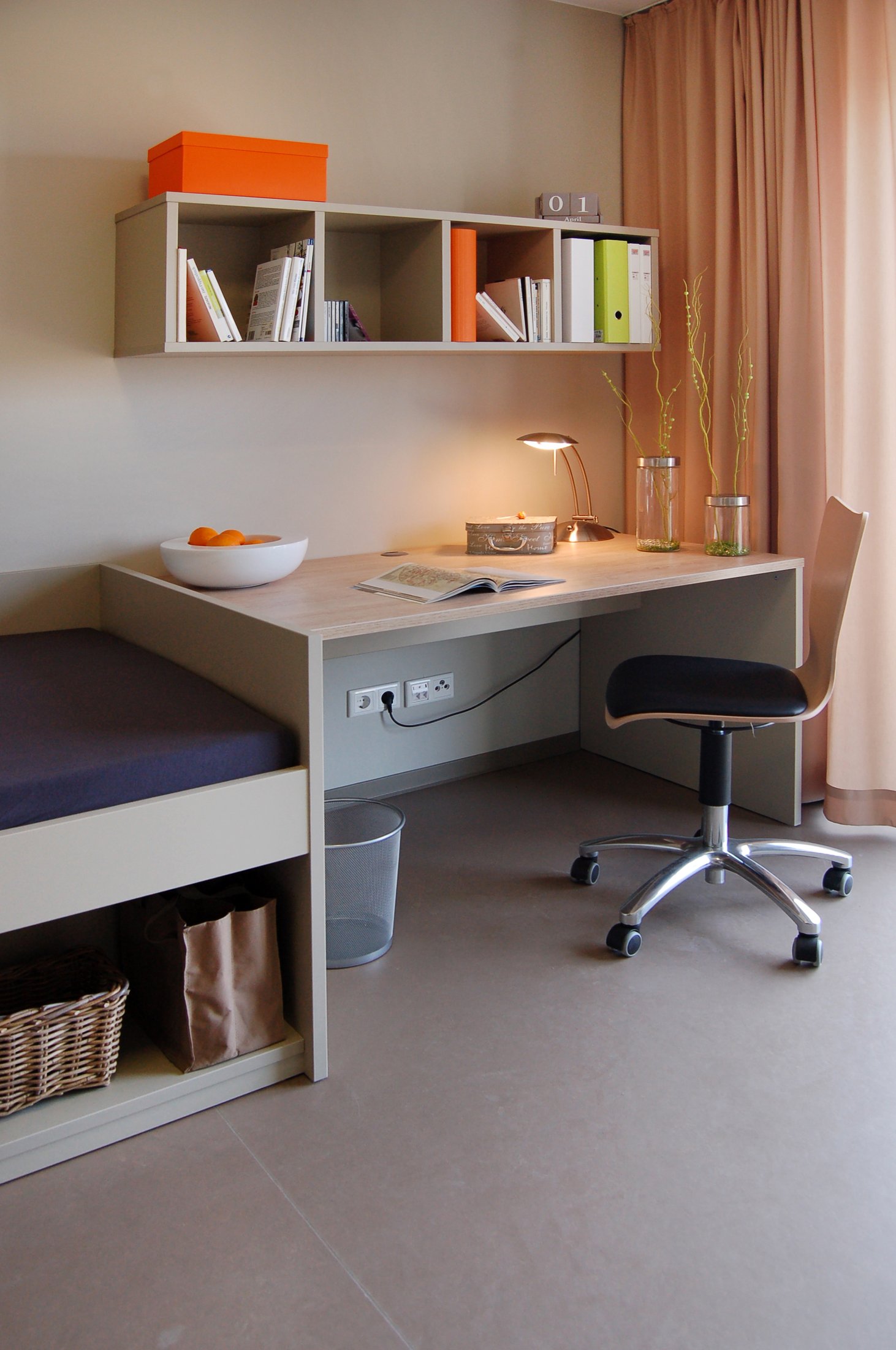 Studierendenwohnheim Paderborn-Alois_Fuchs_Weg: Heller Raum mit Schreibtisch, Bücherregal, Sesseln und dekorativen Elementen.