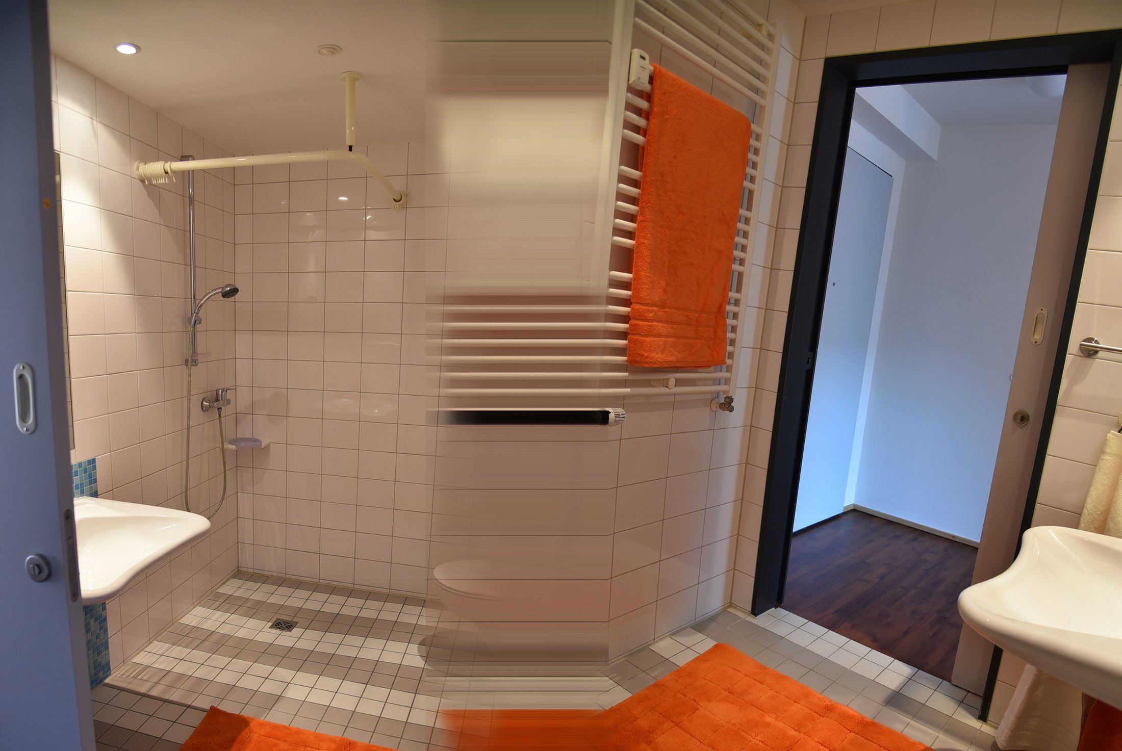 Badezimmer im Studierendenwohnheim Paderborn-Mersinweg_4 mit Dusche, Waschbecken und orangefarbenen Handtüchern.