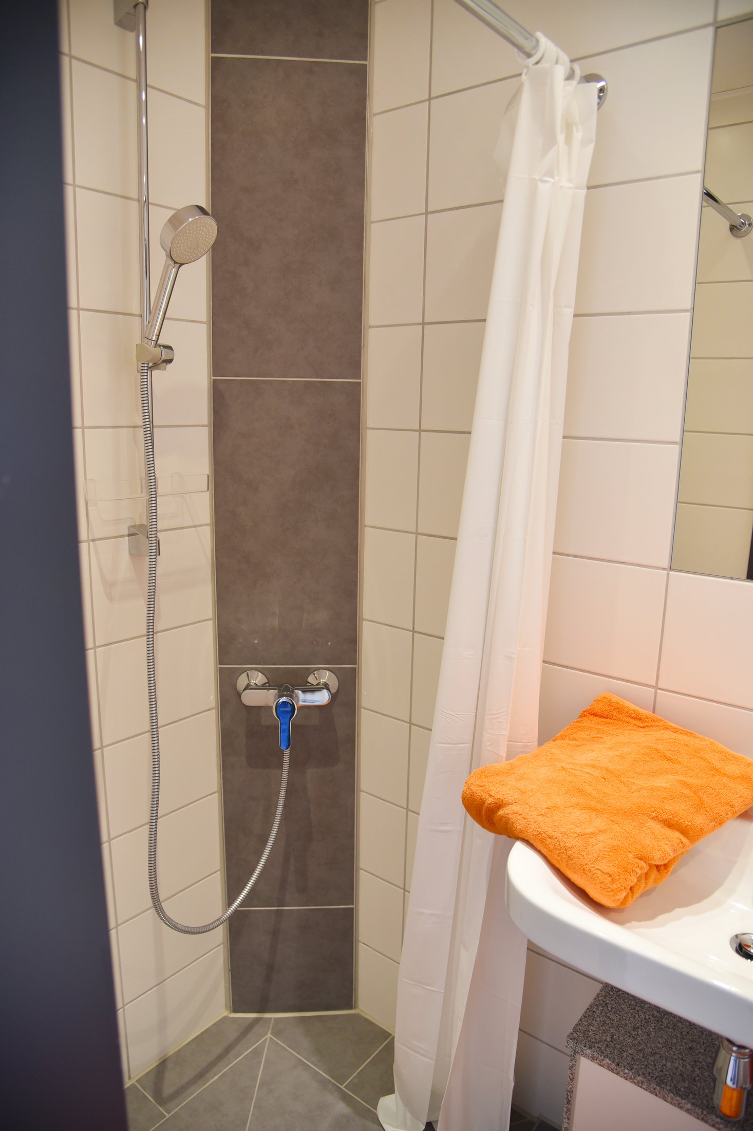 Shower in a student hall of residence in Paderborn-Peter Hille Weg 11, with grey tiles and an orange towel.