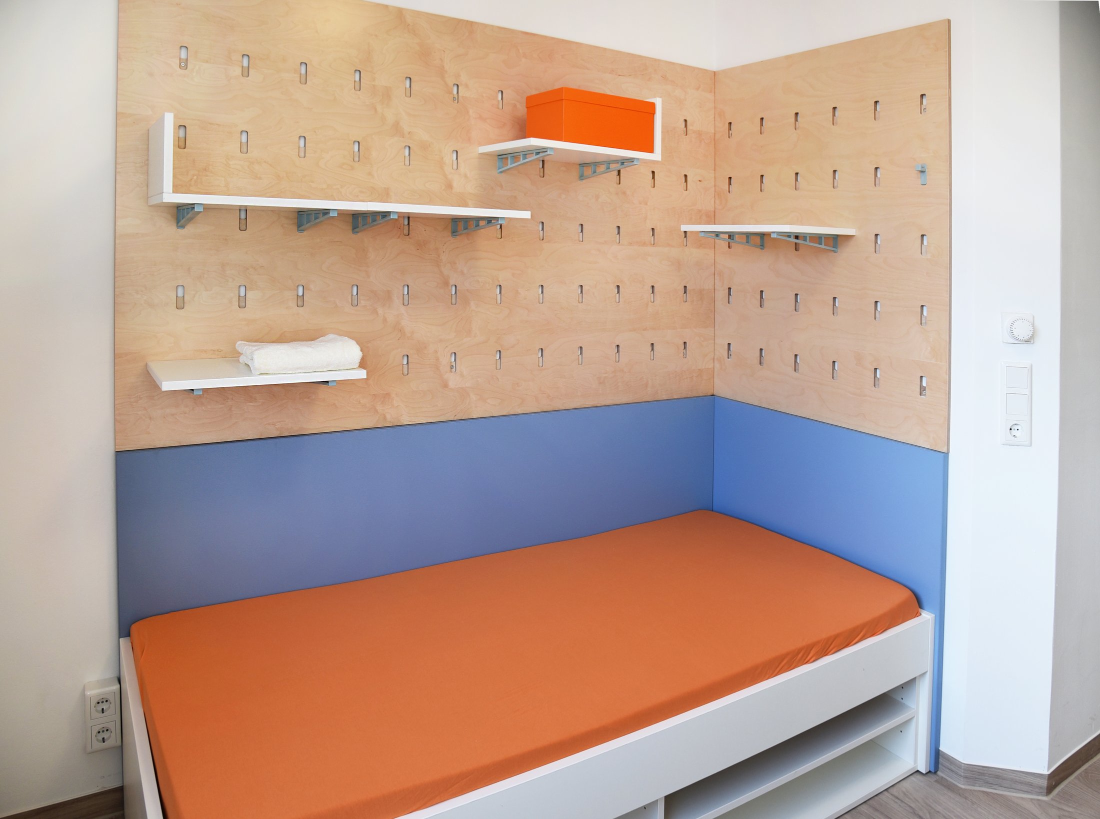 Modern room in a student hall of residence in Paderborn-Peter_Hille_Weg_11 with orange-coloured bed and shelves.