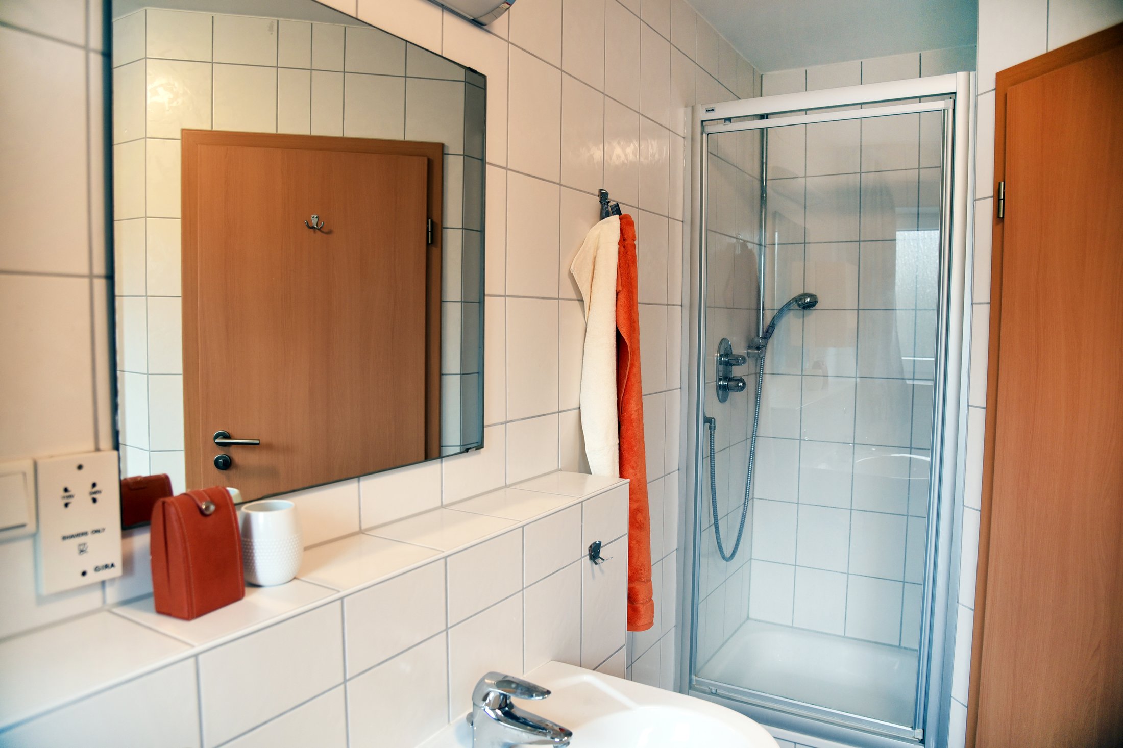 Modernes Badezimmer im Studierendenwohnheim Paderborn-Uhlandstraße mit Dusche, Spiegel und Waschbecken.