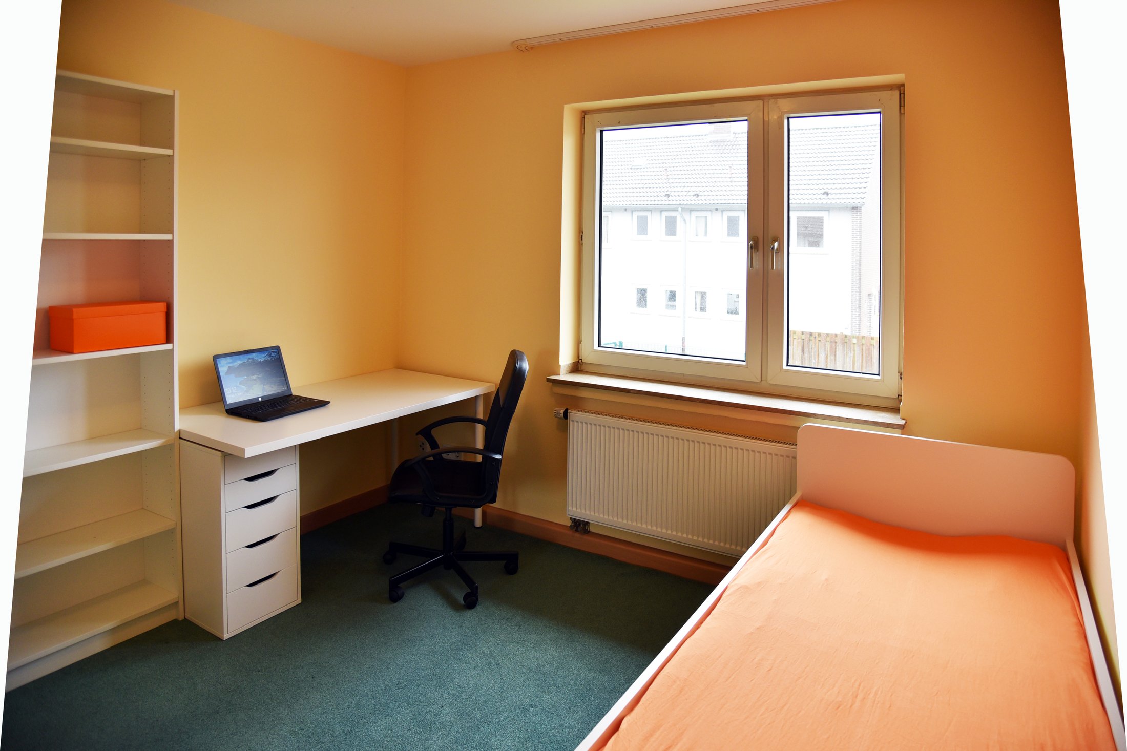 Modernes Zimmer im Studierendenwohnheim Paderborn-Uhlandstraße mit Schreibtisch, Laptop, Regal und Einzelbett.