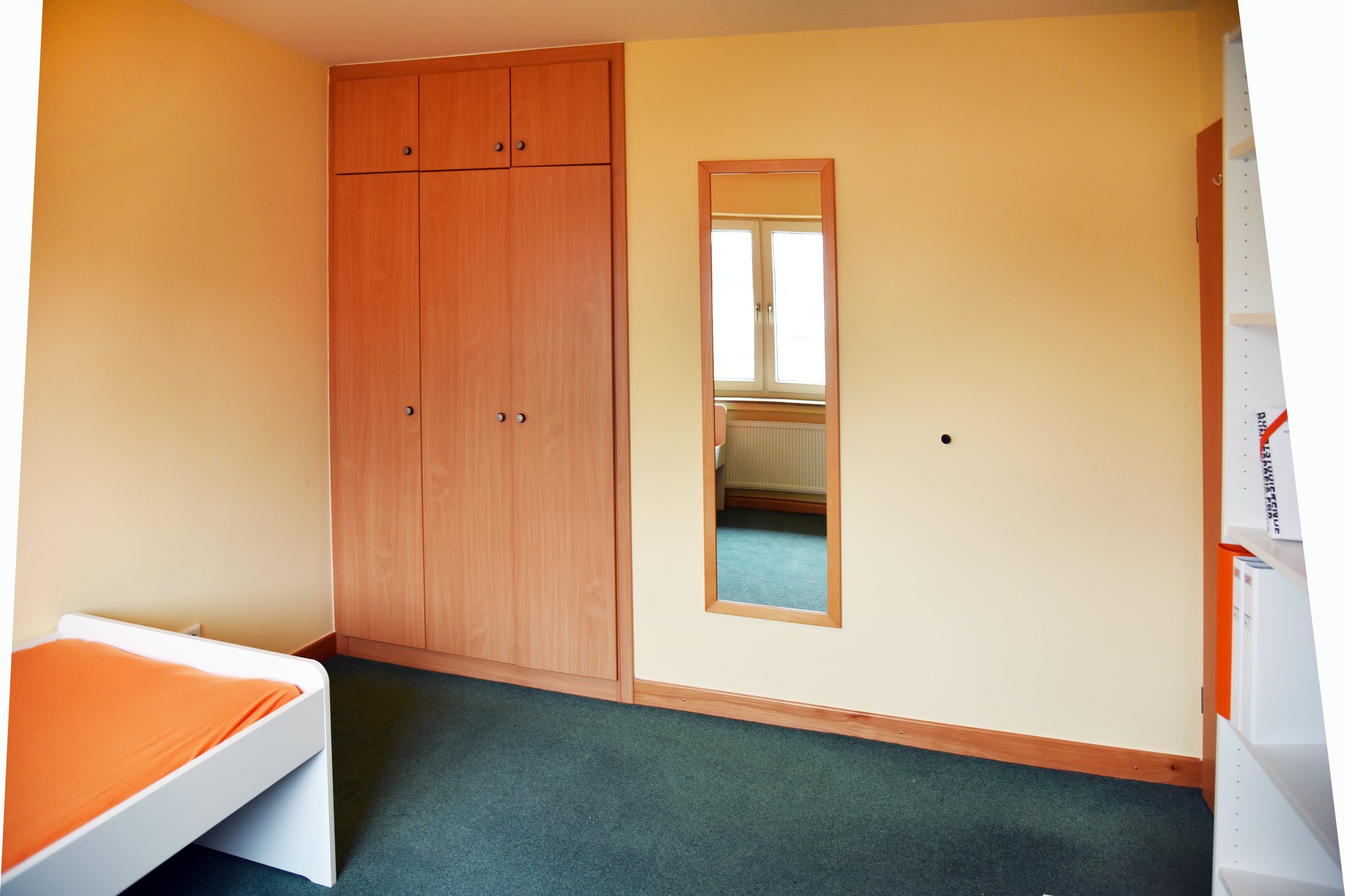 Studierendenwohnheim in Paderborn-Uhlandstraße: Helles Zimmer mit Bett, Kleiderschrank und Spiegel.