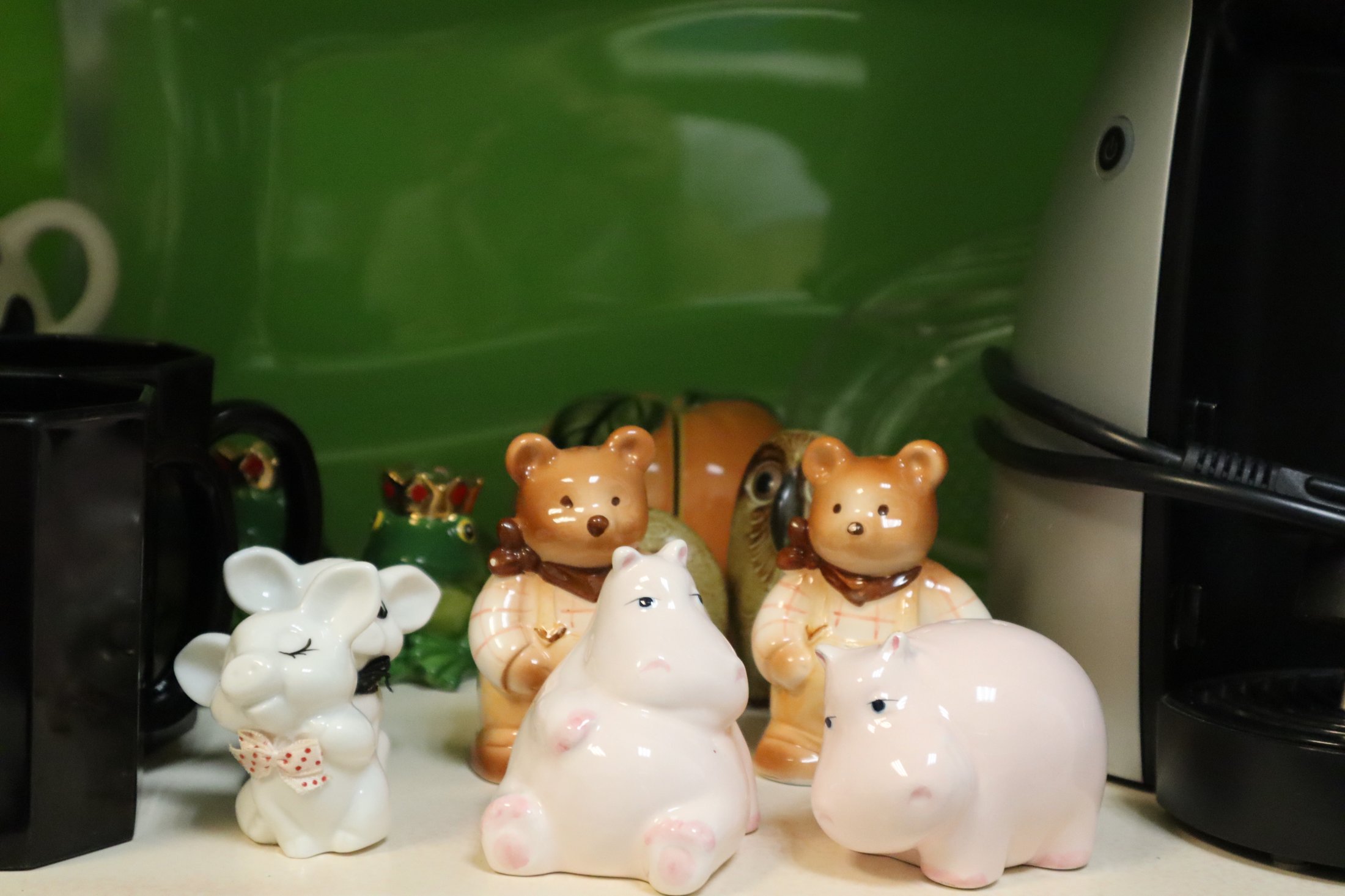 Kleine Figuren von einem weißen Hasen, zwei Bären und einem rosa Nilpferd vor einer grünen Wand und Tassen.