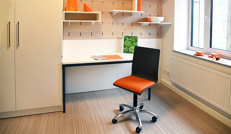 Studierendenwohnheim in Paderborn-Vogeliusweg: Heller Raum mit Schreibtisch und modernen Regalen.